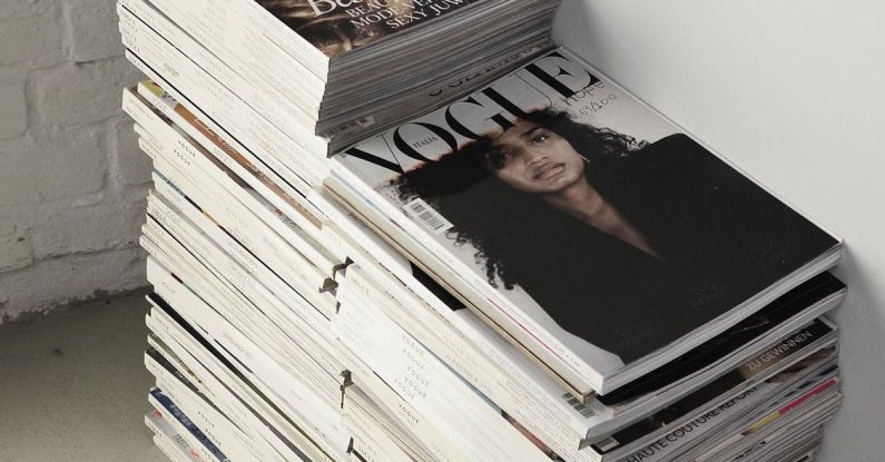 Design Trends - High angle many fashion magazines stacked on floor against white brick wall in studio